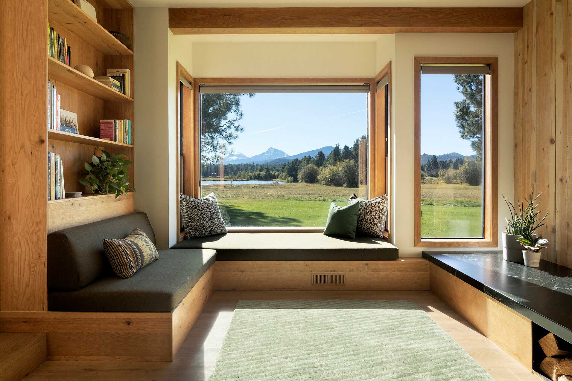 A bay window with bench seating is surrounded by bookshelves and a large fixed picture window at the Bailey Residence in Black Butte Ranch, Oregon.
